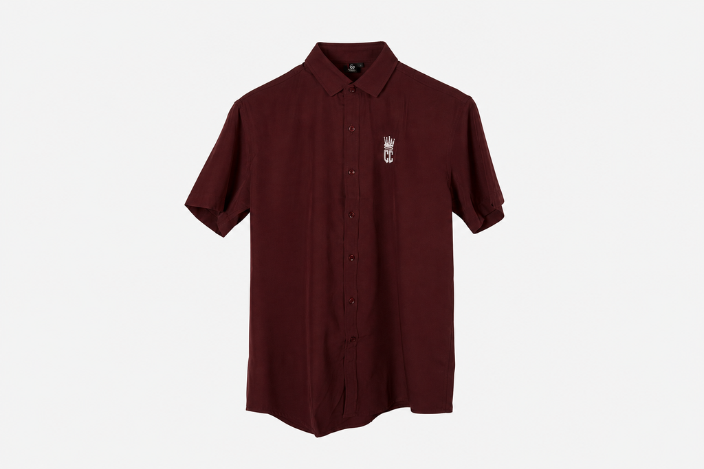A maroon short-sleeve button-up shirt with a small white crown and 'M' logo on the left chest, displayed on a clean white background.