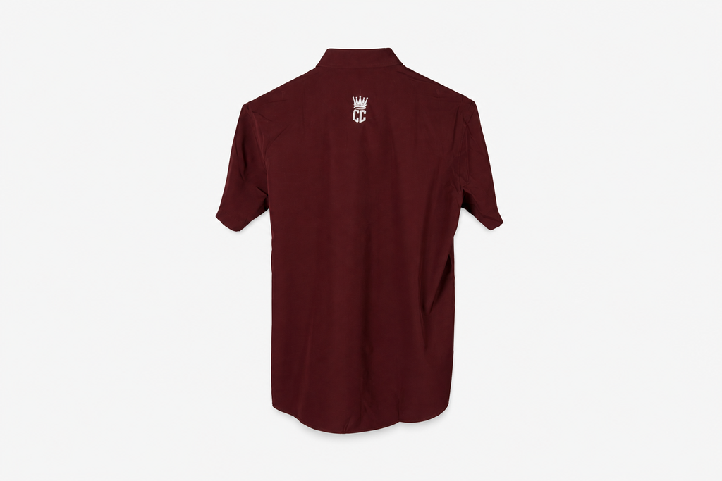 A maroon short-sleeve button-up shirt with a small white crown and 'M' logo on the left chest, displayed on a clean white background.